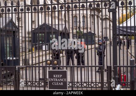 View through railings, armed officers of Protection Command in Specialist Operations of Metropolitan Police on duty guarding Downing Street, London UK.