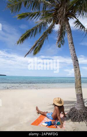 Man with sunhat and curly hair chilling under palm tree at sandy beach Stock Photo