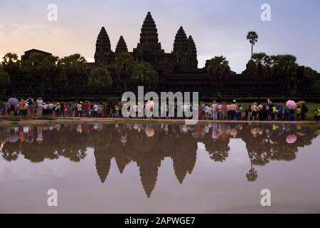 Reflection of Ankor Wat's silhouette and visitors on lake during dawn Stock Photo