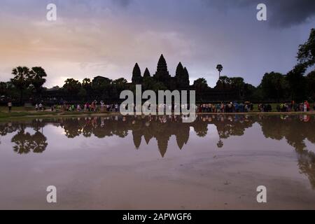 Reflection of Ankor Wat's silhouette and visitors on lake during dawn Stock Photo