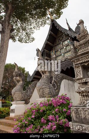 Dragon statue and pink flowers outside dark temple in Wat Chedi Luang