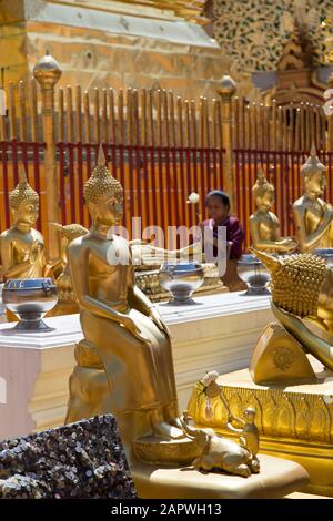 Golden statues and Thai woman praying in background, Wat Doi Suthep Stock Photo