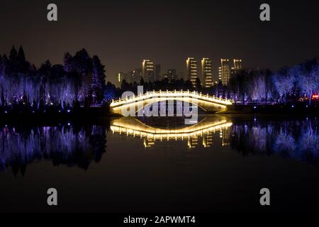 WUHAN, HUBEI / CHINA - NOV 20 2019: Night view of  Chinese bridge with light decoration at East Lake and city skyline on background, Wuhan, Hubei, Chi