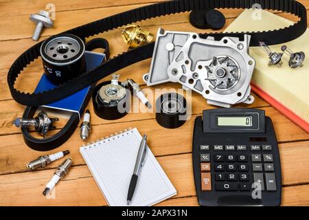 Various car parts with calculator, a block and a ballpoint pencil on the wooden table. Stock Photo