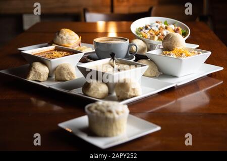 Coffee and food with orange lights in the background. Coffee, Hot chocolate, Salad, Sandwich, Rolls, Cupcakes, and Soup. On a coffee shop table. Stock Photo
