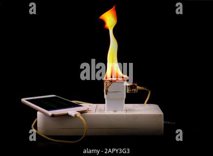 On fire adapter charger mobile at plug Receptacle on black background, Electric short circuit failure resulting in electricity wire burnt Stock Photo