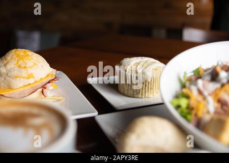 Coffee and food with orange lights in the background. Coffee, Hot chocolate, Salad, Sandwich, Rolls, Cupcakes, and Soup. On a coffee shop table. Stock Photo