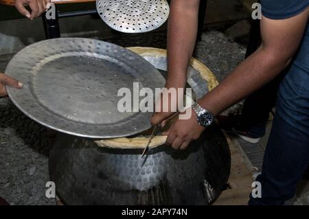 Chef's hands cut bread around an aluminum biriyani pot