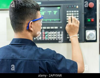 CNC operator, mechanical technician worker at metal machining milling center in tool workshop inserting data with keyboard wearing Stock Photo