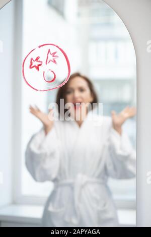 Young woman screaming in front of mirror with shocked face drawn with lipstick Stock Photo