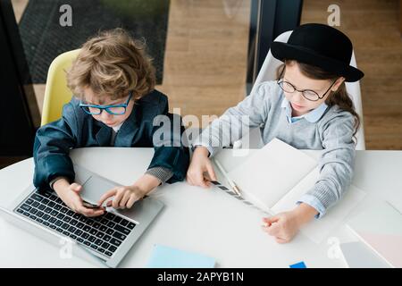 Two diligent busy schoolkids in casualwear sitting by desk and working Stock Photo