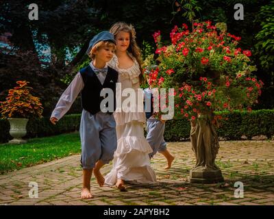 Kids walking through the garden surrounded by bushes and flowers under the sunlight Stock Photo