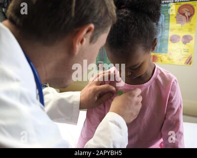 Doctor examining an African-American child with a stethoscope in a hospital Stock Photo