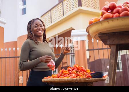 young black woman holding tomatoes and giving thumbs up in the market Stock Photo