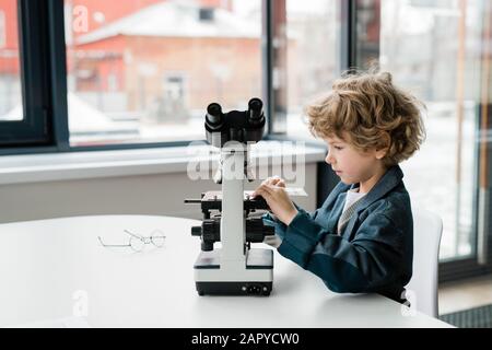 Clever little scientist putting chemical sample in microscope in laboratory Stock Photo