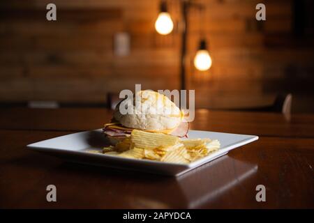 Ham sandwich with potato chips sitting on a dining table. Stock Photo