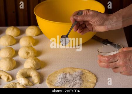 Female hands sprinkle powdered sugar on raw bagel Stock Photo