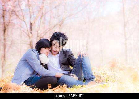 Portrait of beautiful young couple sitting on ground in park relaxing Stock Photo