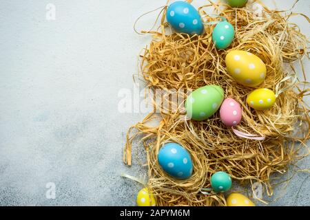 Easter holiday card concept with colored eggs and straw on concrete background with copy space Stock Photo