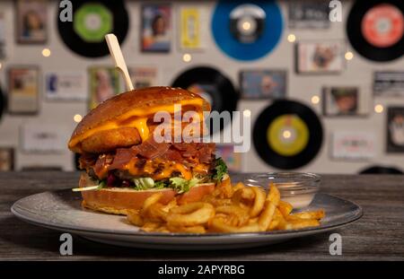 Homemade beef burger with battered brie cheese, cheddar sauce, serrano ham with french fries on wooden table. isolated image. Stock Photo