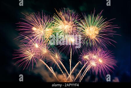 Beautiful colorful fireworks display on the urban lake for celebration on dark  background. Explosion of fireworks at night. Stock Photo
