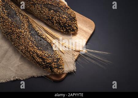 Homemade sourdough bread baguette on vintage towel on black background. Stock Photo
