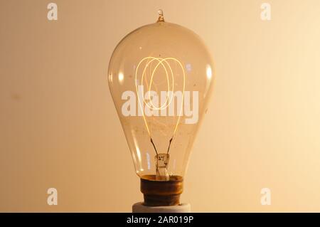 A very old lightbulb with a carbon filament lit on a low current. Stock Photo