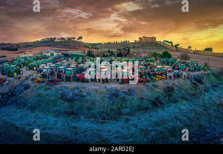 Dozens of green, red tractors lined up in a farm courtyards on a freezing January day under the castle of Belmonte Spain Stock Photo