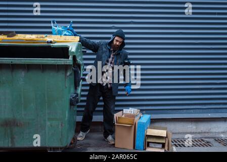 Bearded bum searching food in trashcan on street Stock Photo