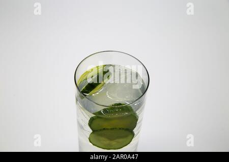 Top view on isolated glass with sparkling tonic water, cucumber slices, gin and ice cubes, white gray background Stock Photo