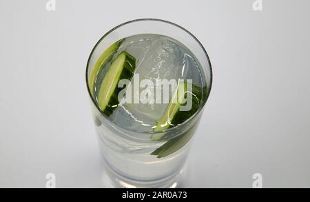 Top view on isolated glass with sparkling tonic water, cucumber slices, gin and ice cubes, white gray background Stock Photo