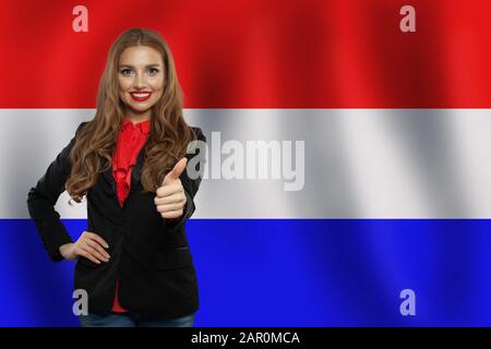Love Netherlands! Happy cute woman smiling and showing thumb up on netherlandish flag background Stock Photo