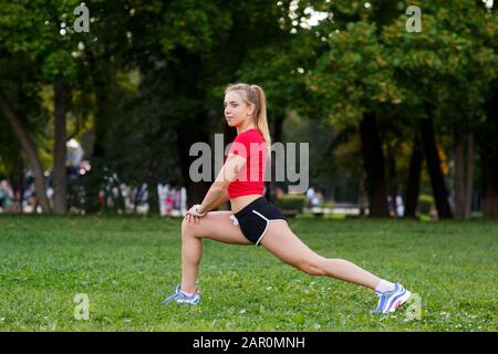 Girl doing lunges. Young slim woman doing lunges in a city park. Outdoors Sports. Healthy lifestyle concept. Morning exercises. Stock Photo