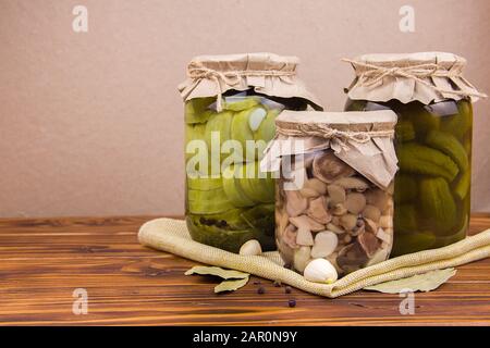 fermented pickled canned zucchini and cucumber mushrooms in jars garlic bay leaf black pepper peas on a piece of burlap on a brown wooden background Stock Photo