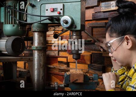 Women standing is craft working drill wood at a workbench with Drill Press power tools at carpenter machine in the workshop Stock Photo