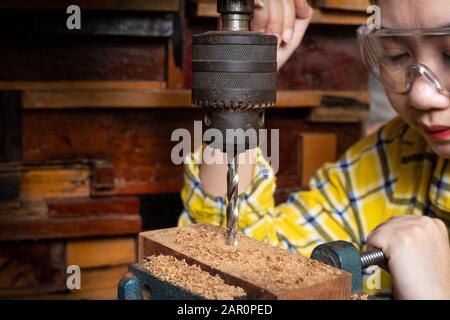 Women standing is craft working drill wood at a workbench with Drill Press power tools at carpenter machine in the workshop Stock Photo