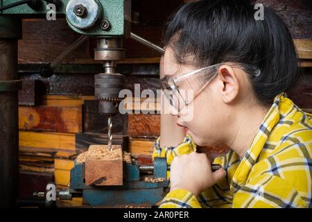 Women standing is craft working drill wood at a workbench with Drill Press power tools at carpenter machine in the workshop Stock Photo