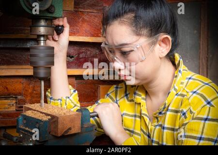 Women standing is craft working drill wood at a workbench with Drill Press power tools at carpenter machine in the workshop Stock Photo