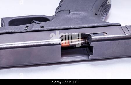 A black 9mm semi automatic pistol on it's side with an opened slide showing a 9mm bullet through the ejection port on a white background Stock Photo