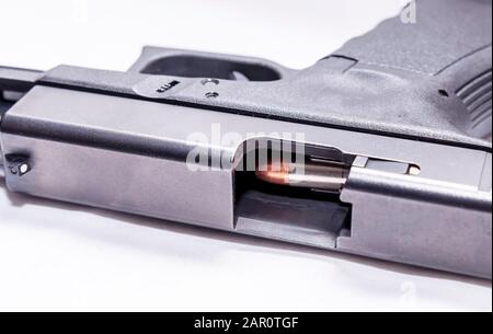 A black 9mm semi automatic pistol on it's side with an opened slide showing a 9mm bullet through the ejection port on a white background Stock Photo