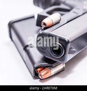 A black 9mm semi automatic pistol with a loaded pistol magazine with a single 9mm hollow point bullet on a white background Stock Photo