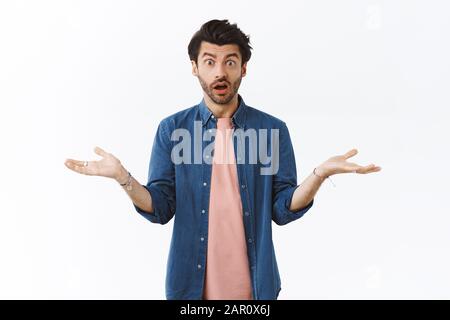 Surprised and confused young man cant understand what happened, shrugging and spread hands sideways indecisive, stare distressed and upset, open mouth Stock Photo