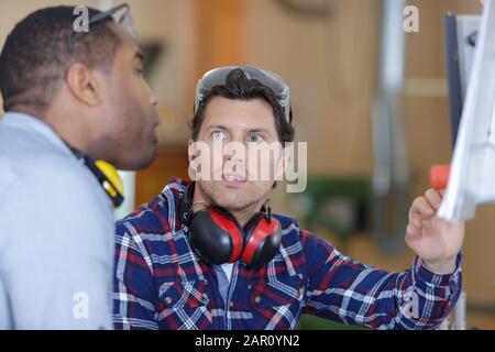 male engineers with technical drawing operating cnc machine in factory Stock Photo