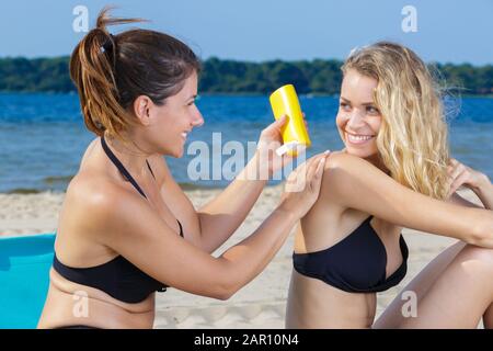 Best friends applying sunscreen girl rubbing suntan lotion on back