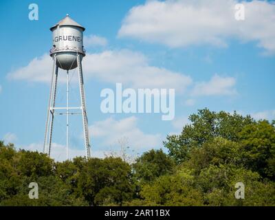 Metal water tank of small texas town Gruene standing high above trees on sunny day. Clouds and blue sky in background. Copyspace available, no people. Stock Photo