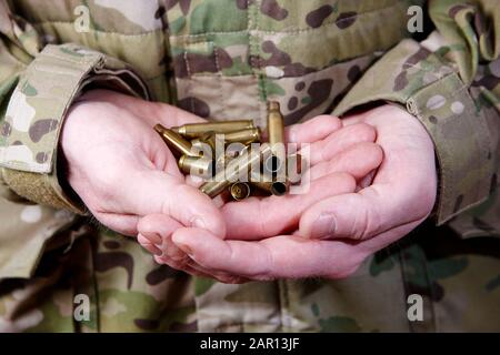 man in combat fatigues holding spent used shell cartridges in the palms of his hands Stock Photo