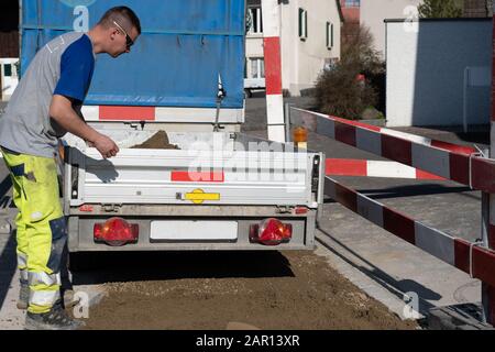 Young Pipeline technician on construction site closes tailgate of a trailer loaded with sand. young construction worker; Man; Trailer; Pendant; constr Stock Photo