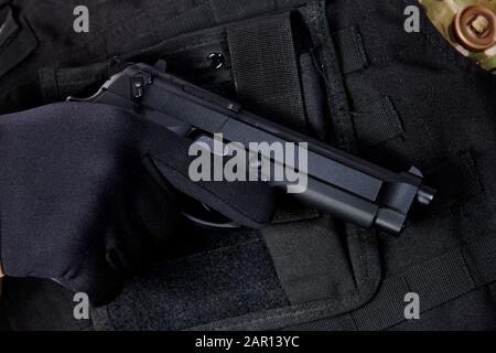 man wearing bullet proof jacket with gloved hand holding beretta semi automatic pistol ,military militia concept private security contractor armed gun Stock Photo