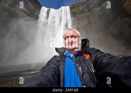 mid 40s grey haired single male tourist takes awkward selfie at skogafoss waterfall iceland Stock Photo