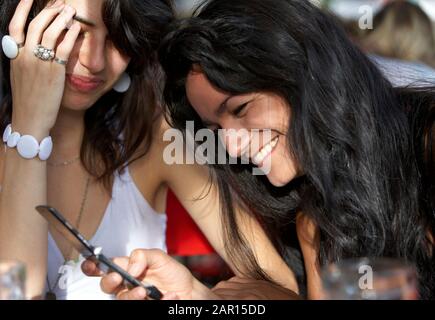 two young hispanic 20s women laughing over a text on screen app message mobile phone buenos aires argentina  Model released image Stock Photo